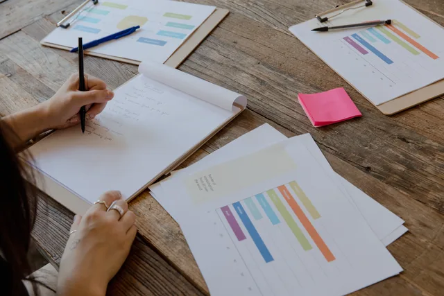 Hands writing on paper with colorful charts on wooden table, organized workspace. Selecting creator discovery software: a manual baseline register and six independent gates