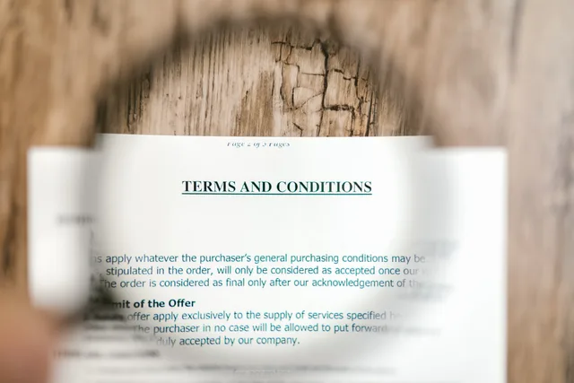 Magnifying glass focusing on terms and conditions document on wooden surface. Creator discovery platforms: six legal and contract checks before you choose a supplier, from Companies House to PECR