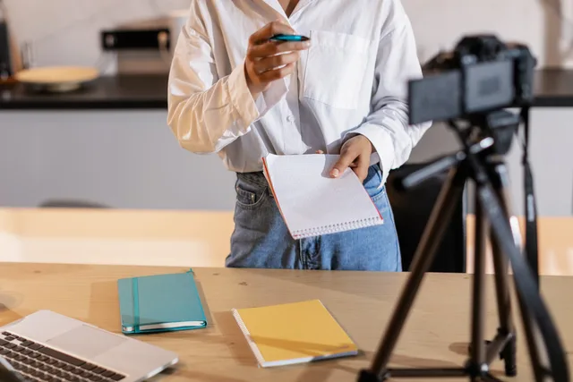 Vlogger recording content with a camera, holding notes and using a laptop in a modern setting. Five season peaks that shape UK creator discovery timing